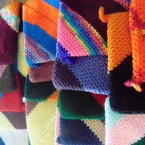 May include: A stack of colorful crocheted squares in various patterns and colors, including purple, pink, blue, green, orange, red, and brown.
