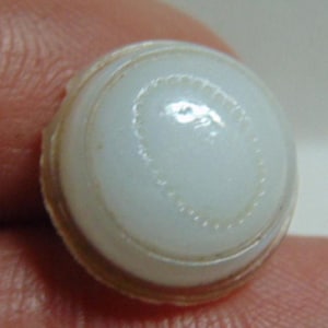 May include: A white button with a concentric circle design. The button has a smooth, glossy finish and a slightly raised edge.