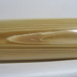May include: A close-up of a light brown wooden cylinder with a smooth, polished surface. The wood grain is visible and has a light beige color.