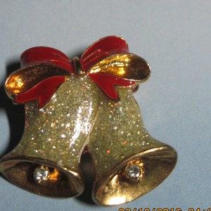 May include: Gold-tone Christmas bells with a red and gold bow. The bells are covered in glitter and have a clear rhinestone on each.