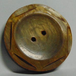 May include: A round, vintage button with a carved geometric design. The button is primarily a warm, golden-brown color with two small holes for sewing. The center has a slightly lighter, metallic hue.