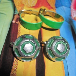 May include: A pair of green and silver clip-on earrings with a geometric design. The earrings are round and have a raised, textured surface.