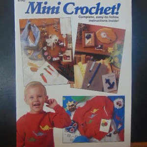 May include: A book titled "Mini Crochet!" with a white background and colorful images of crocheted items. The book cover features a child wearing a red sweater with a crocheted bird design, and a variety of other crocheted items, including a bag, a toy train, and a picture frame.