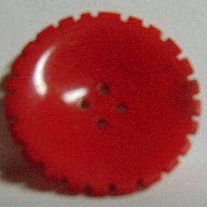 May include: A bright red plastic button with four holes. The button has a scalloped edge.