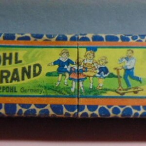 May include: A rectangular box with a blue and white spotted pattern. The box features a central panel with the words "POHL BRAND" and an illustration of children. The box also has the text "Made by POHL Germany" and a harp symbol.