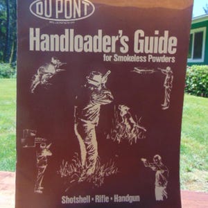 May include: A vintage "DuPont Handloader's Guide" for smokeless powders, dated 1975-76. The cover is brown with white illustrations of people shooting guns and the words "Shot Shell, Rifle, Handgun".