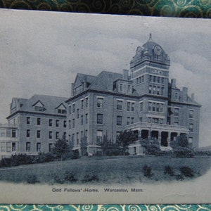 May include: Vintage postcard featuring the Odd Fellows' Home in Worcester, Massachusetts. The image shows a large, multi-story brick building with a prominent clock tower. The postcard is in grayscale, with the text "Odd Fellows' Home, Worcester, Mass."