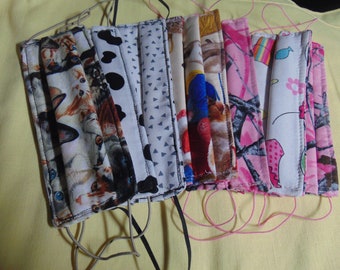 May include: A collection of 10 handmade fabric face masks with various patterns, including cats, geometric designs, and camouflage. The masks are all sewn with pink thread and have elastic ear loops.
