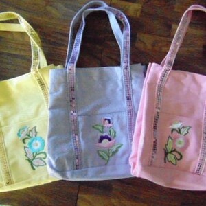 May include: Three tote bags with floral embroidery. The bags are yellow, lavender, and pink. Each bag has a sequined trim.