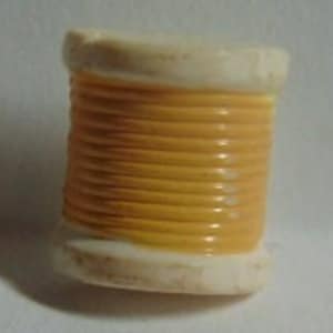 May include: A small, ceramic spool of thread. The thread is a vibrant yellow, wrapped around a cream-colored base. The spool is a miniature representation of a sewing supply.