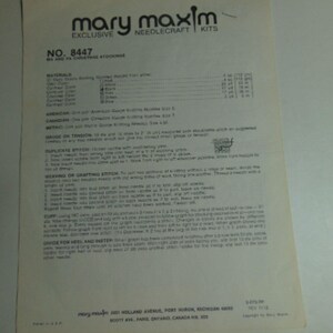 May include: A cream-colored Mary Maxim needlecraft kit instruction sheet for Ma and Pa Christmas stockings, model number 8447. The document contains printed text detailing materials, knitting gauge, duplicate stitch, and weaving instructions.