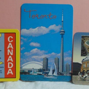 May include: Three colorful postcards featuring images of Canada. The first postcard shows a map of Canada with the provinces and territories labeled. The second postcard shows the CN Tower in Toronto, Ontario. The third postcard shows the Olympic Stadium in Montreal, Quebec.