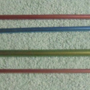 May include: A set of four long, slender crochet hooks in a variety of metallic colors, including red, blue, green, and pink. Each hook features a smooth, cylindrical shaft with a curved hook at one end, designed for yarn craft projects.