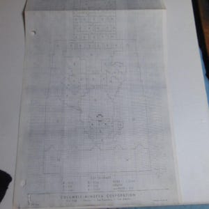 May include: A white paper craft pattern sheet from Columbia-Minerva Corporation featuring a black grid design with various lettered sections and a key to chart at the bottom. The document includes instructions for eyes, mouth, and nose, with a folded top edge.