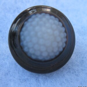 May include: A black button with a white center. The center is textured with small white dots.