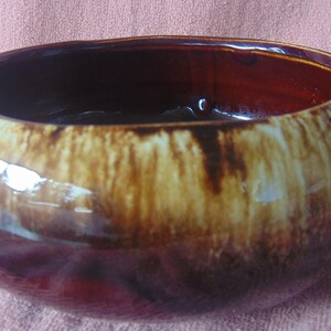 May include: A brown and white glazed ceramic serving bowl with two handles. The bowl has a rustic, hand-crafted look.