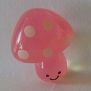 May include: A pink mushroom with white polka dots and a smiling face. The mushroom is made of a soft, pliable material.