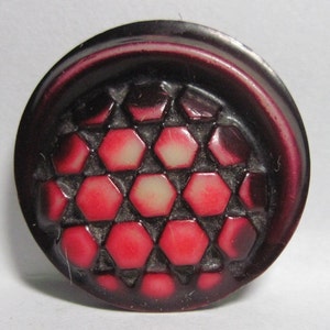 May include: A dark red button with a raised design of a honeycomb pattern in shades of red and white.