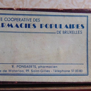 May include: A vintage cardboard box with a white label that reads "SOCIETE COOPERATIVE DES PHARMACIES POPULAIRES - DE BRUXELLES" and "R. PONSAERTS, pharmacien Chaussée de Waterloo, 99. Saint-Gilles - Téléphone 37.00.80".