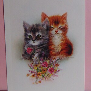 May include: Two kittens, one grey and one orange, are sitting together. The grey kitten is holding a single pink rose. Both kittens are surrounded by a bouquet of colourful flowers.