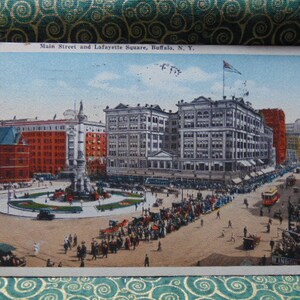 May include: A vintage postcard depicting a street scene in Buffalo, New York. The postcard shows Main Street and Lafayette Square, with a large building in the background and a crowd of people in the foreground. The text on the postcard reads "Main Street and Lafayette Square, Buffalo, N.Y."