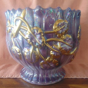 May include: A large iridescent purple ceramic planter with gold floral details. The planter has a scalloped rim and a wide base.