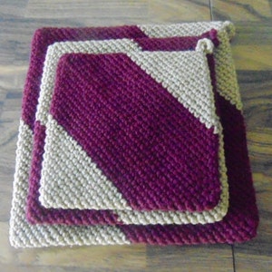 May include: Three crocheted pot holders in a chevron pattern. The largest pot holder is beige with a burgundy chevron pattern. The middle pot holder is burgundy with a beige chevron pattern. The smallest pot holder is beige with a burgundy chevron pattern.