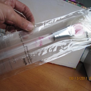 May include: A clear plastic bag containing a silver makeup brush with a pink handle. The brush is labeled "snow duster" and "mark."