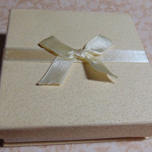 May include: A small, cream-colored gift box with a satin ribbon tied in a bow.