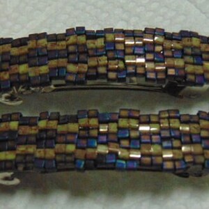 May include: Two hair clips made of small, iridescent, square beads in shades of blue, purple, brown, and yellow. The beads are arranged in a checkered pattern.