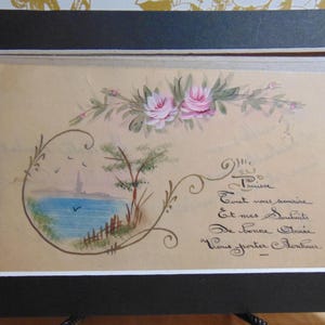 May include: A vintage postcard with a hand-painted image of a seascape with a small town in the distance. The postcard features a floral design with pink roses and green leaves. The text on the postcard reads "Tout vous sourire et mes souhaits de bonne année vous porter bonheur."
