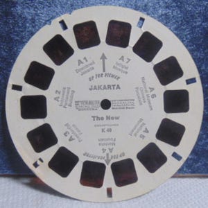 May include: A circular white View-Master reel featuring seven pairs of dark film frames. The center is printed with 'JAKARTA', 'The New', 'K 49', and various landmark labels including 'Downtown Jakarta', 'Istiqlal Mosque', and 'Presidential Palace'.