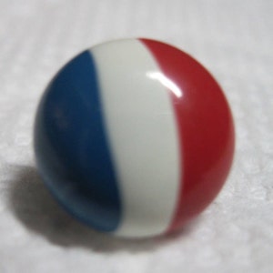 May include: A round, glossy button with a red, white, and blue striped design. The button is a patriotic theme.