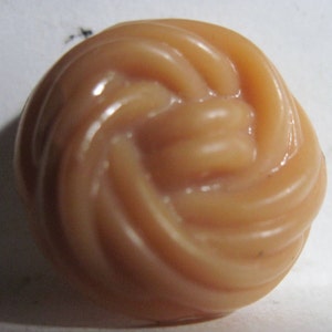 May include: A close-up of a light peach-colored button with a swirled design. The button has a glossy finish and a rounded shape. The design resembles a knot or a spiral.