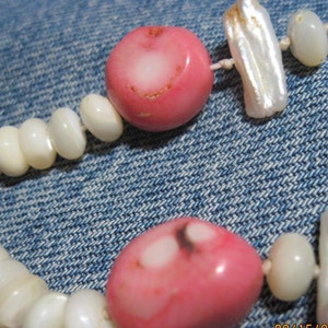 May include: A pink and white beaded necklace with a mix of round and rectangular beads. The necklace is made of natural materials and has a rustic, handmade look.