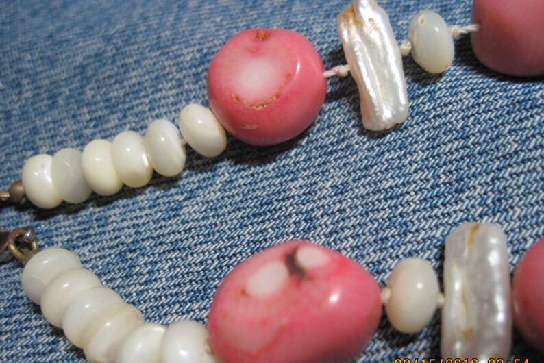 May include: A pink and white beaded necklace with a mix of round and rectangular beads. The necklace is made of natural materials and has a rustic, handmade look.