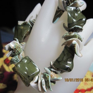 May include: A green and white shell bracelet with a textured, iridescent finish. The bracelet is made of natural shells and is strung together with a strong cord.