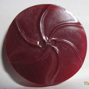 May include: A dark red plastic button with a swirl design and two holes.