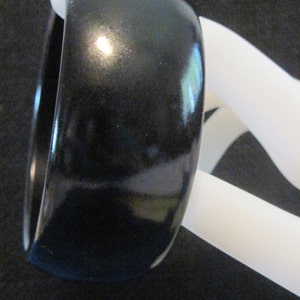 May include: A black, glossy, round bangle bracelet.