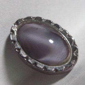 May include: A silver oval-shaped pendant with a purple iridescent stone set in the center. The pendant has a decorative border.