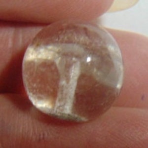 May include: A clear glass marble with a white swirl design inside. The marble has a translucent appearance.