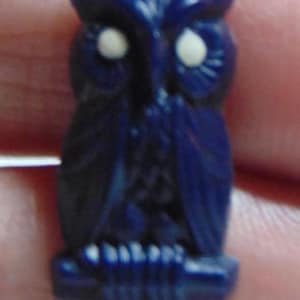 May include: A dark blue owl figurine with white eyes. The owl is perched on a branch and has a detailed design.