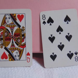 May include: Two playing cards: the Queen of Hearts and the Eight of Spades. The Queen card features a detailed illustration with red, yellow, and black accents. The Eight of Spades card displays eight black spade symbols.