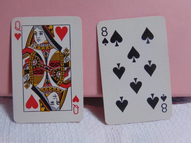 May include: Two playing cards: the Queen of Hearts and the Eight of Spades. The Queen card features a detailed illustration with red, yellow, and black accents. The Eight of Spades card displays eight black spade symbols.