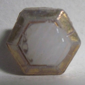 May include: A white octagonal bottle stopper with a gold rim. The stopper has a smooth, slightly iridescent surface.