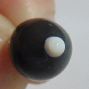 May include: A black glass marble with a white dot in the center.