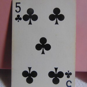 May include: A standard playing card with a white background and black ink. The card is a five of clubs. The number "5" is in the top left corner and the bottom right corner of the card. There are five black clover symbols on the card.
