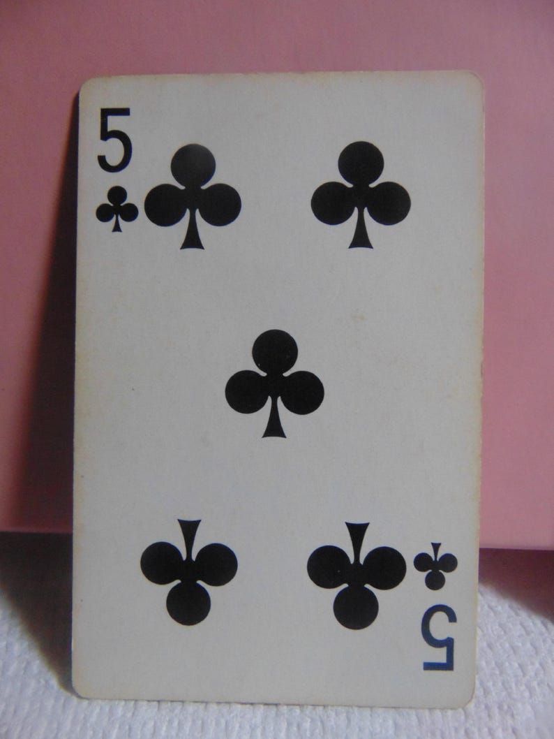 May include: A standard playing card with a white background and black ink. The card is a five of clubs. The number "5" is in the top left corner and the bottom right corner of the card. There are five black clover symbols on the card.