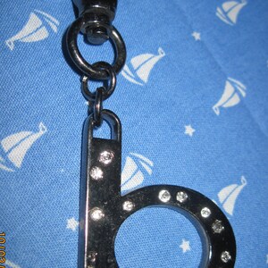 May include: A silver keychain with a letter 'B' charm. The charm is decorated with small rhinestones. The keychain has a silver clip.