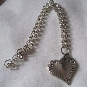 May include: A silver chain necklace with a heart-shaped pendant. The pendant has a detailed design and a smooth, polished finish.